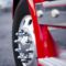 The powerful front wheel on the steering axle of the truck on a powerful modern aluminum wheels with chrome mounting bolts. Detail of a red truck with a wing and chrome complements the steps of the magnitude of this giant.